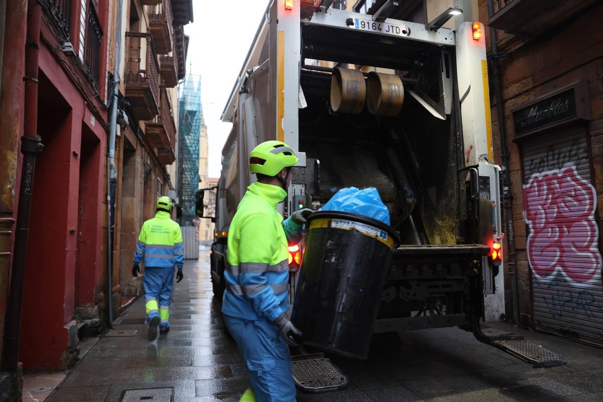 Un operario trasladando los residuos de un cubo negro al camión.