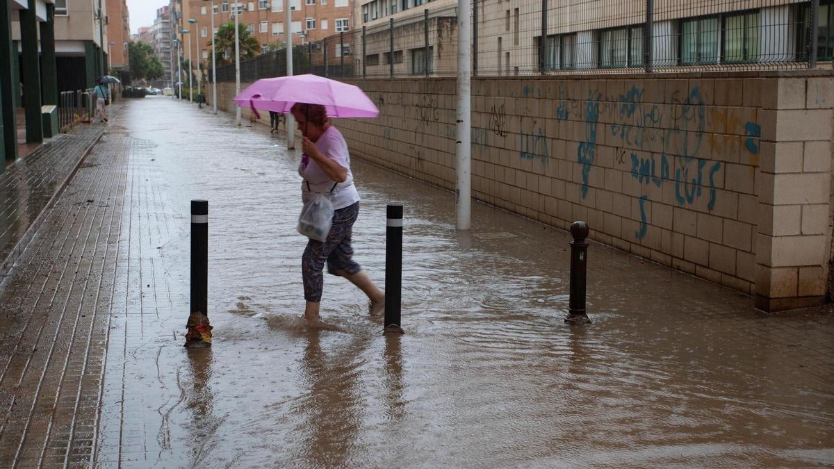 Una dona travessa un carrer negat per la pluja en una imatge d’arxiu