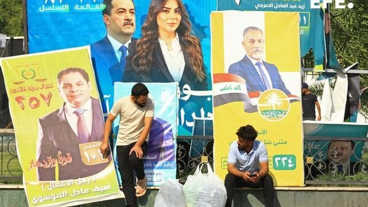 Dos iraquíes sentados en una calle de Bagdad con carteles electorales a sus espaldas.