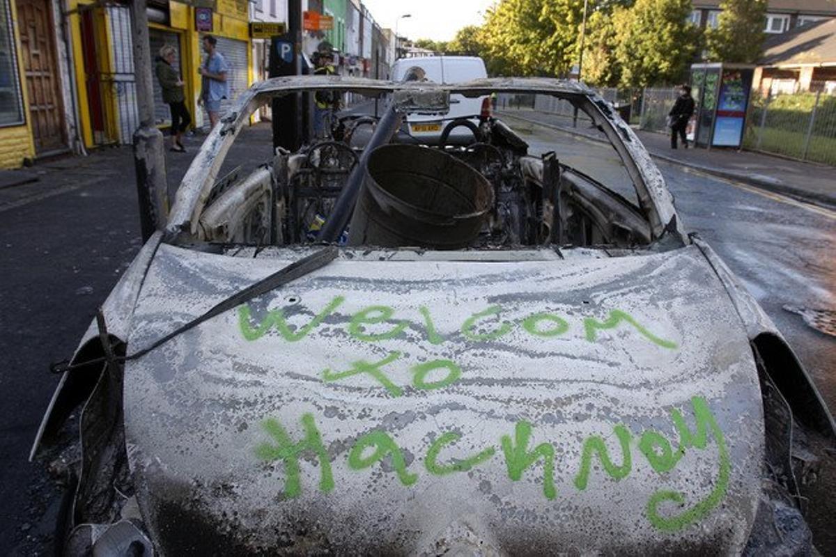 Un cotxe incendiat durant els disturbis d’ahir a la nit en què es pot llegir una pintada amb Benvinguts a Hackney.