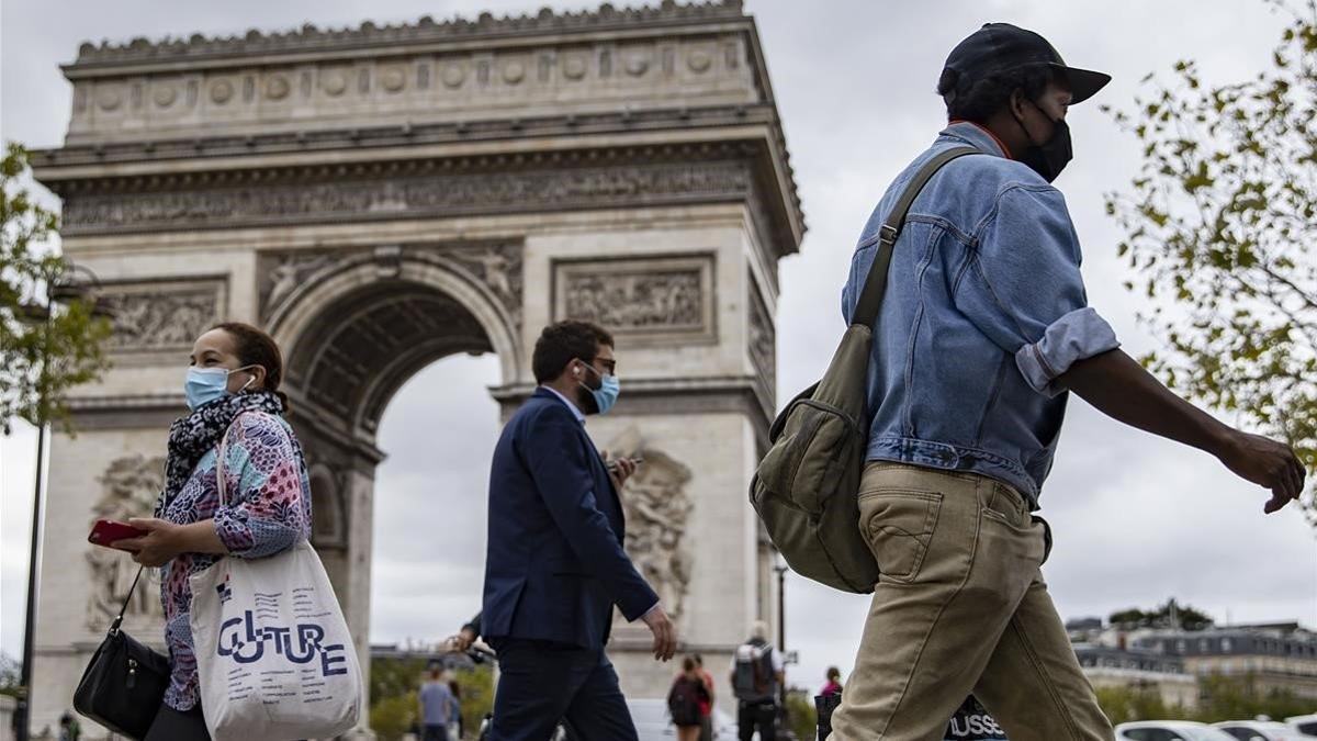 Parisinos con mascarilla caminan por los Campos Elíseos, con el Arco de Triunfo detrás, este viernes.