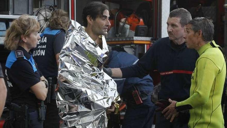 El bañista, envuelto en una manta térmica, recriminado por el bombero que le rescató, en presencia de policías locales.