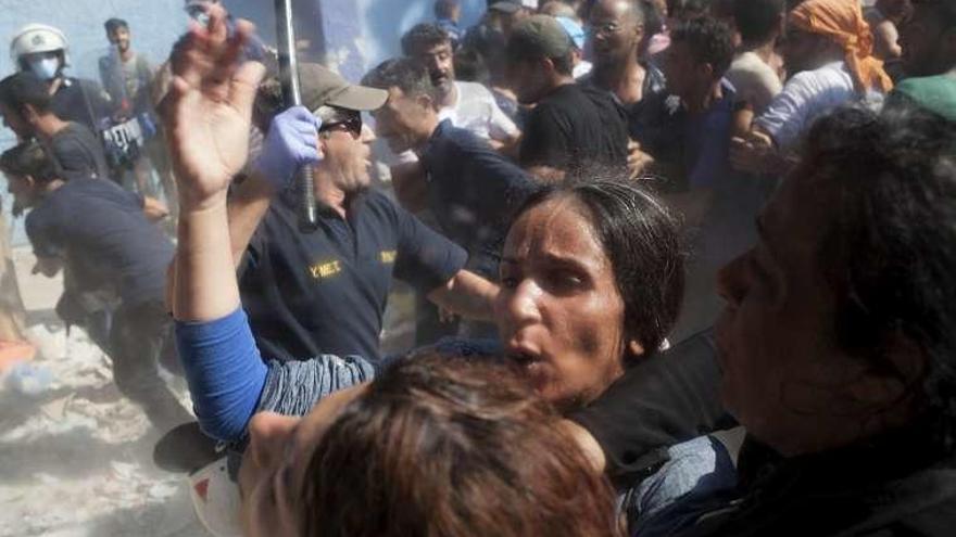 Un policía blande la porra ante inmigrantes en la isla de Lesbos. // Reuters