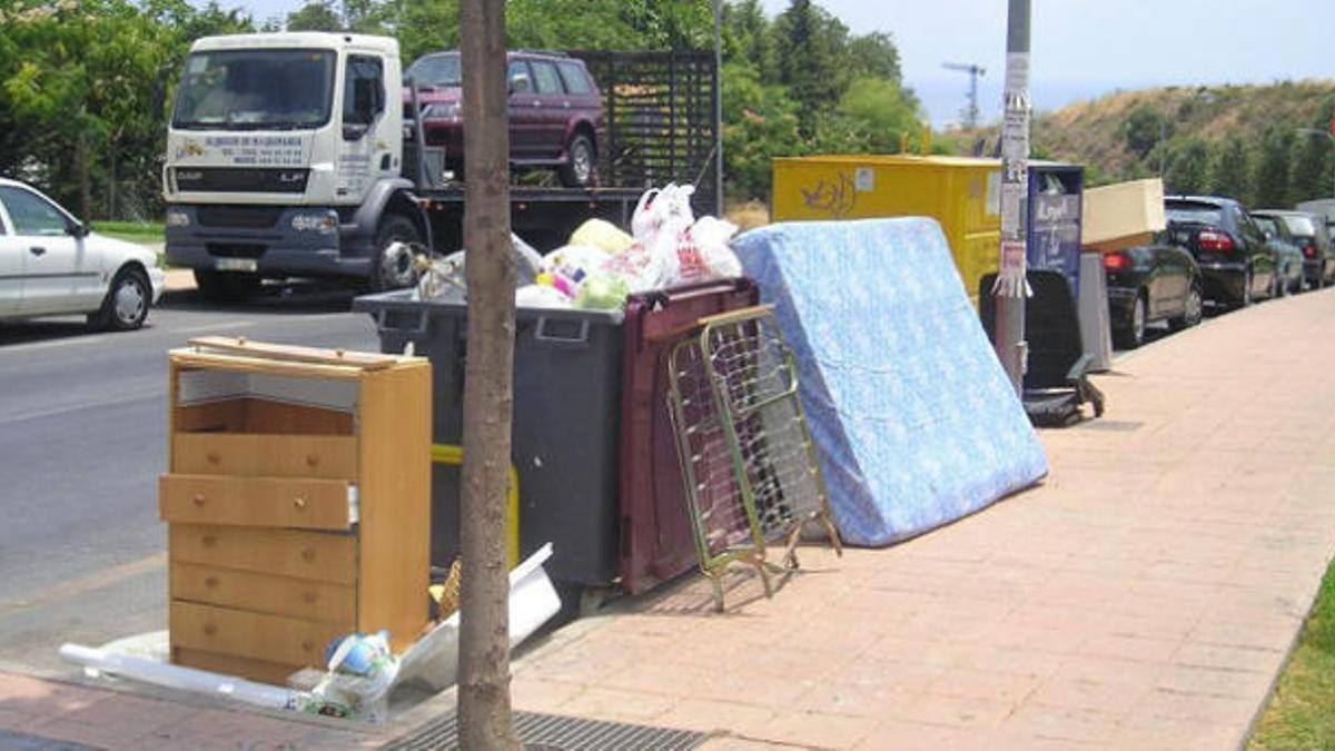 Muebles amontonados junto a un contenedor en la vía pública