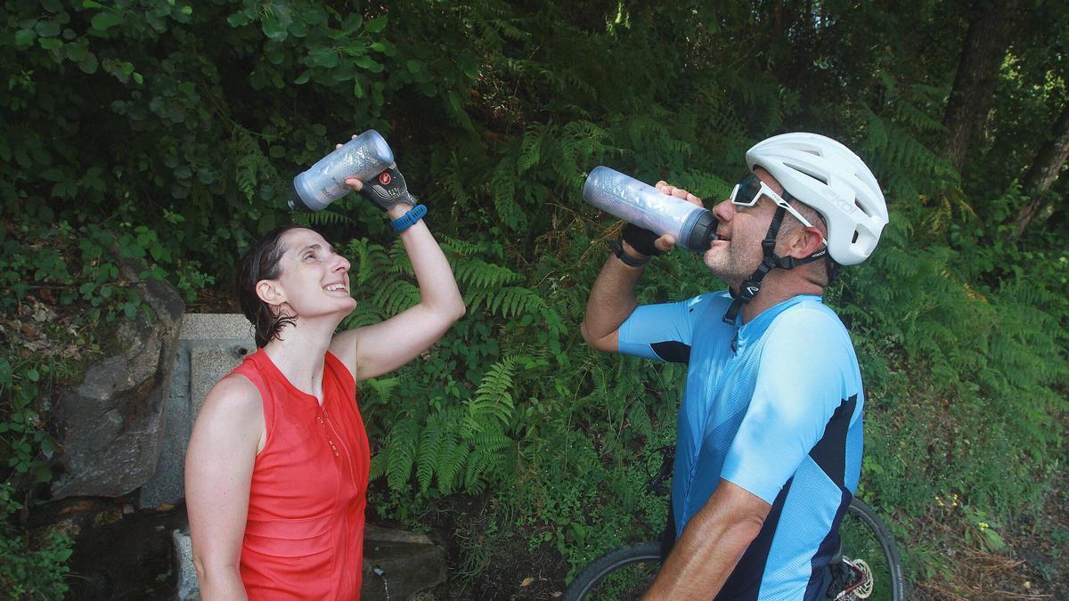 Dos ciclistas se refrescan en una fuente de Ourense ante las altas temperaturas de esta ola de calor de junio.