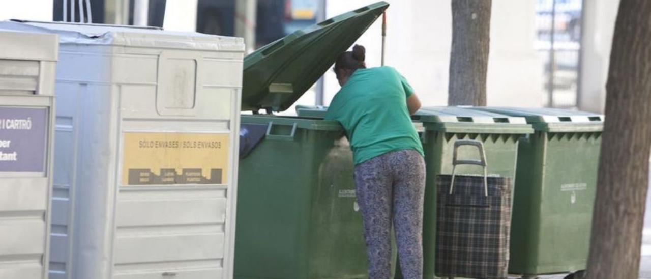 Una mujer revisa un contenedor depositado en la calle, en una imagen de archivo. | LEVANTE-EMV