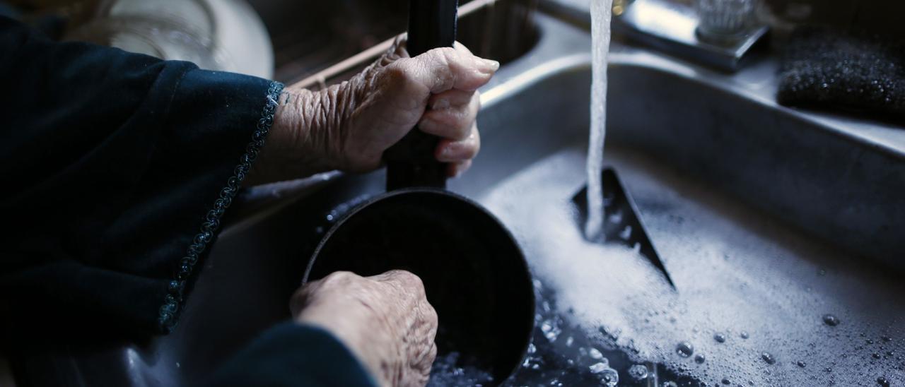 Un fregadero con el grifo de agua abierto y el usuario limpiando un utensilio.