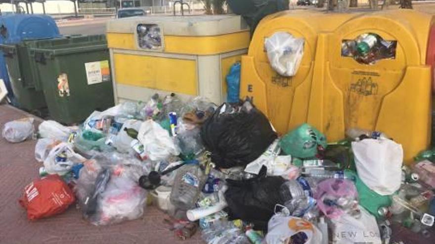 Residuos para reciclar, acumulados junto a contenedores llenos.