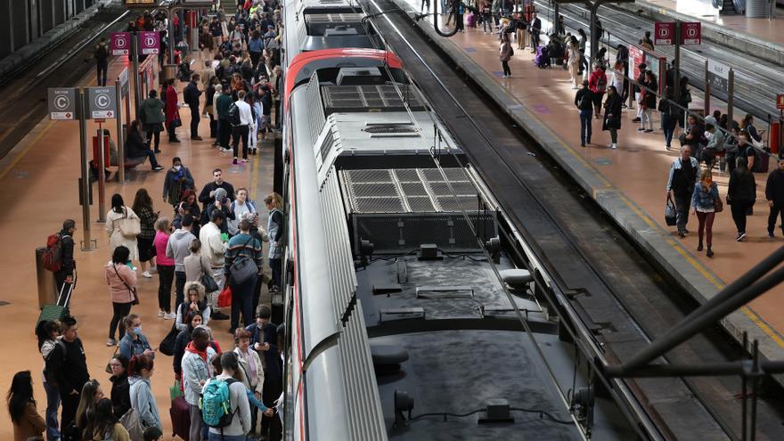 Numerosas personas con maletas esperan en el andén la salida de un tren, en la estación Almudena Grandes-Atocha Cercanías