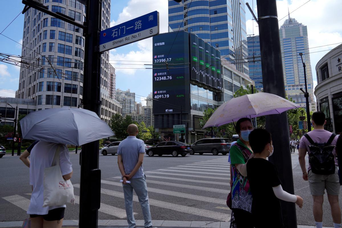 Ciudadanos transitan ante carteles con los índices de la bolsa en Shanghai (China).