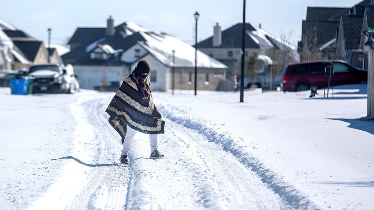 Una persona camina entre la nieve, cubierta con una manta, en Pflugerville, en Texas.