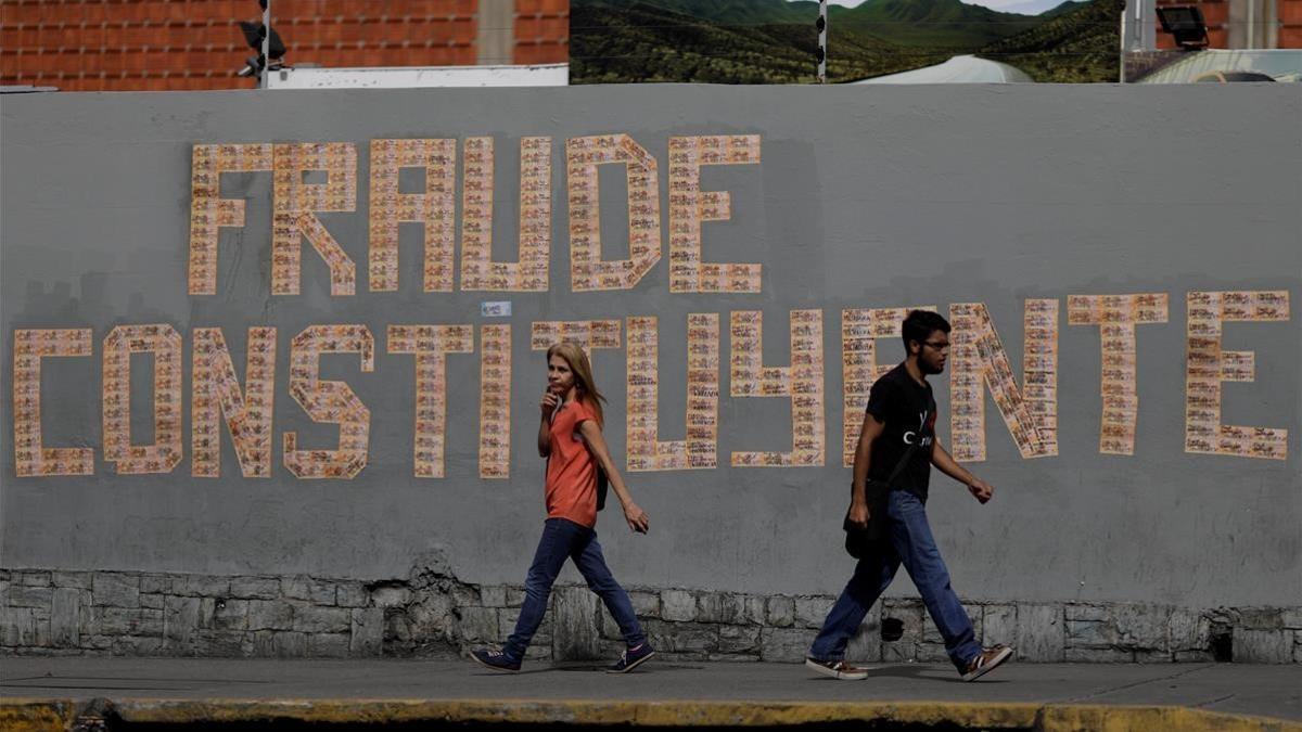 Dos personas pasan junto a un grafito contrario a las elecciones constituyentes, en Caracas, el 26 de julio.