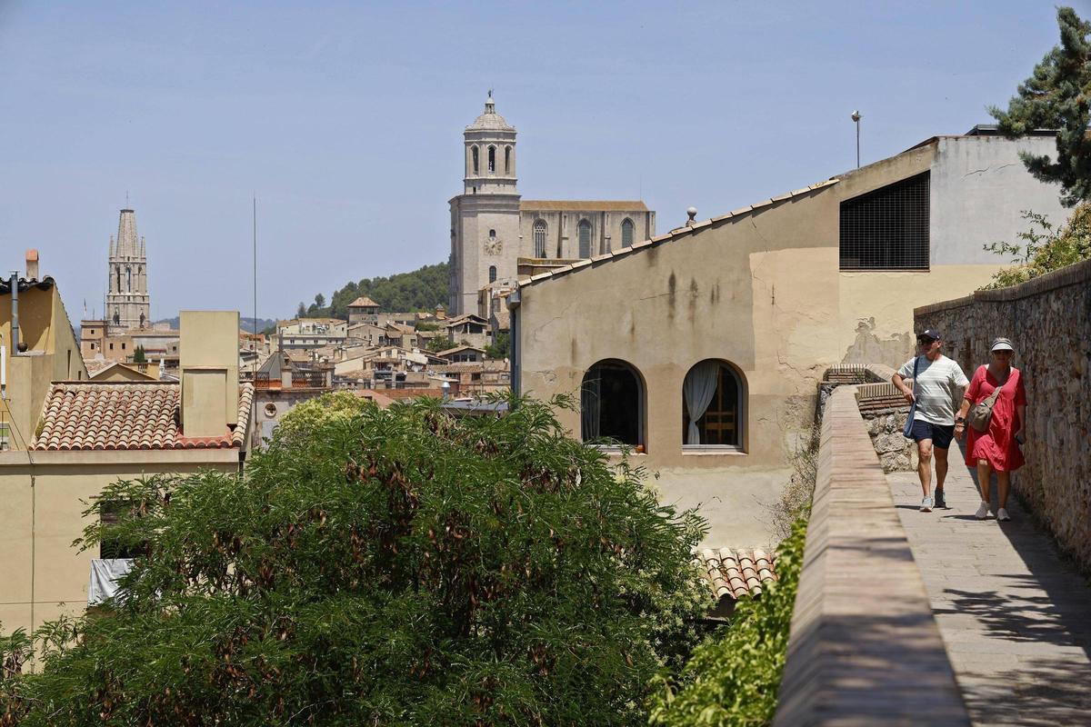 Dos turistes passejant per la muralla de Girona amb Sant Fèlix i la Catedral al fons.