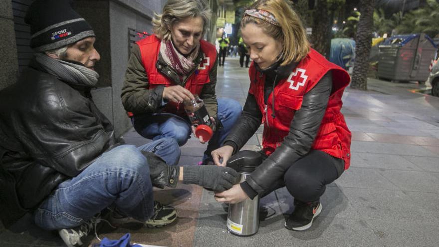 Voluntarias de Cruz Roja reparten bebida caliente a un hombre que pernocta en la calle.