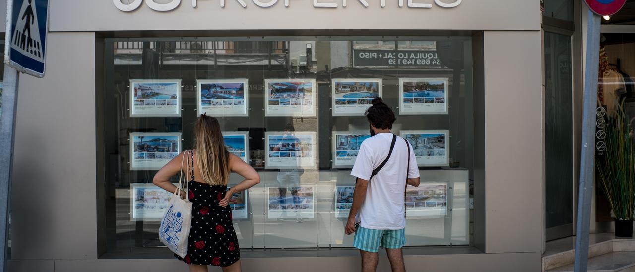 Archivo - Dos personas observan inmuebles en alquiler y en venta en un escaparate de una inmobiliaria ubicada en Palma