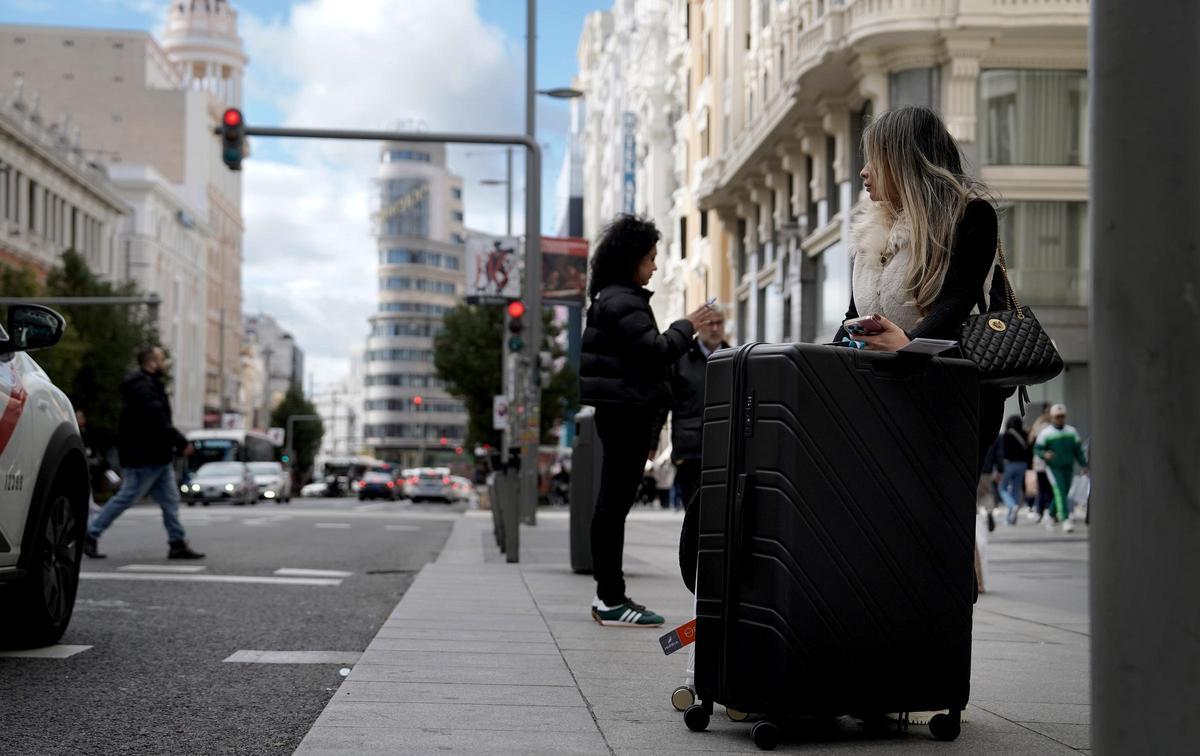 Una turista latina espera un taxi en Gran Vía tras comprar una maleta en el Primark.