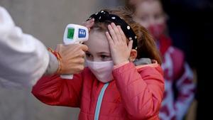 una profesora le toma la temperatura a su alumna, a la entrada del centro escolar.