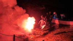 Migrantes llegados en patera a la Colònia de Sant Jordi el pasado sábado lanzan una bengala sobre las rocas para desembarcar