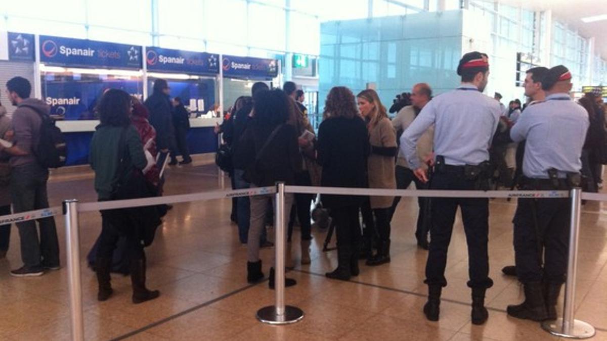 Dos agentes de los Mossos d'Esquadra observan a varios pasajeros ante los mostradores de Spanair, este sábado, en El Prat.