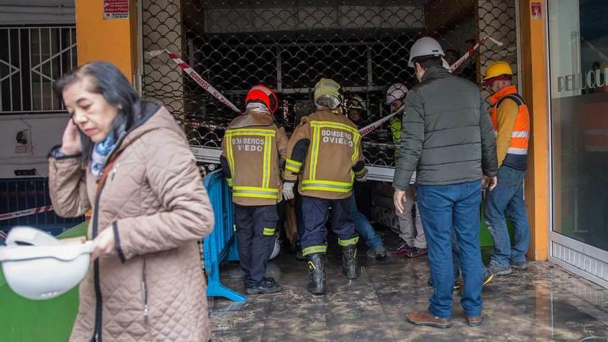 Los bomberos de Oviedo, ayer, levantando la persiana del bazar chino para permitir la revisión de las bajantes de agua corriente y las tuberías.