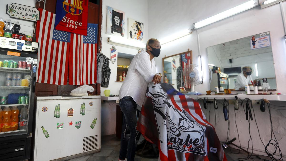 El barbero Germán espera clientes en su local decorado con banderas estadounidenses y una del Barça, en La Habana.