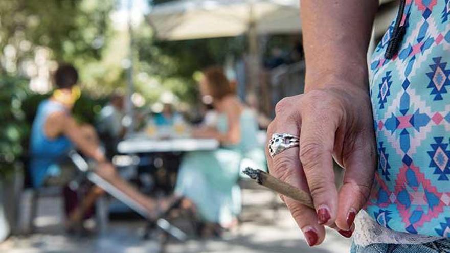 Una mujer, fumando en Palma con una terraza al fondo.