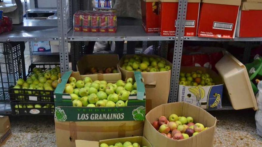 En primer plano, las cajas de manzanas donadas; al fondo, dos voluntarias colocando alimentos.