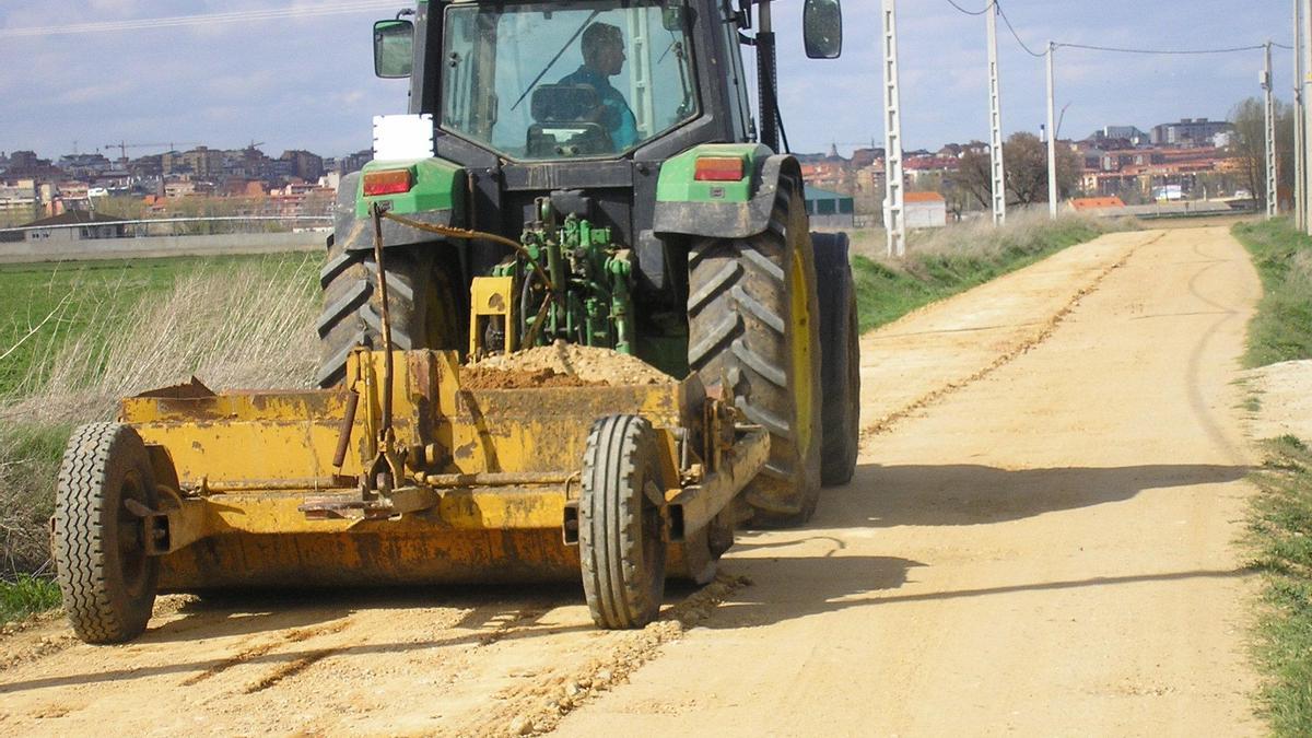 Un tractor repara el firme de un camino rural.