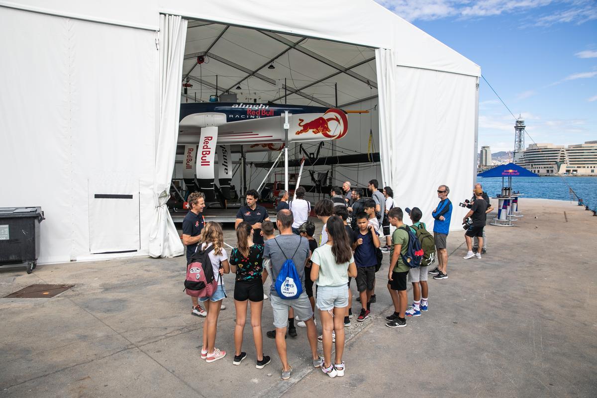 Los miembros del equipo Alinghi Red Bull Racing Matías Buhler y Willy Losa explican las características de los AC40 a los niños y niñas de la Escola Mediterrània de la Barceloneta en el marco del programa 'Viu la vela', para acercar la Copa América a los jóvenes.