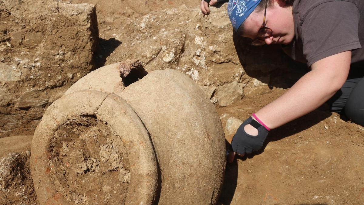 En primer terme, una dolia que s'ha trobat a la zona de producció; al fons, una arqueòloga de la UdG netejant-la