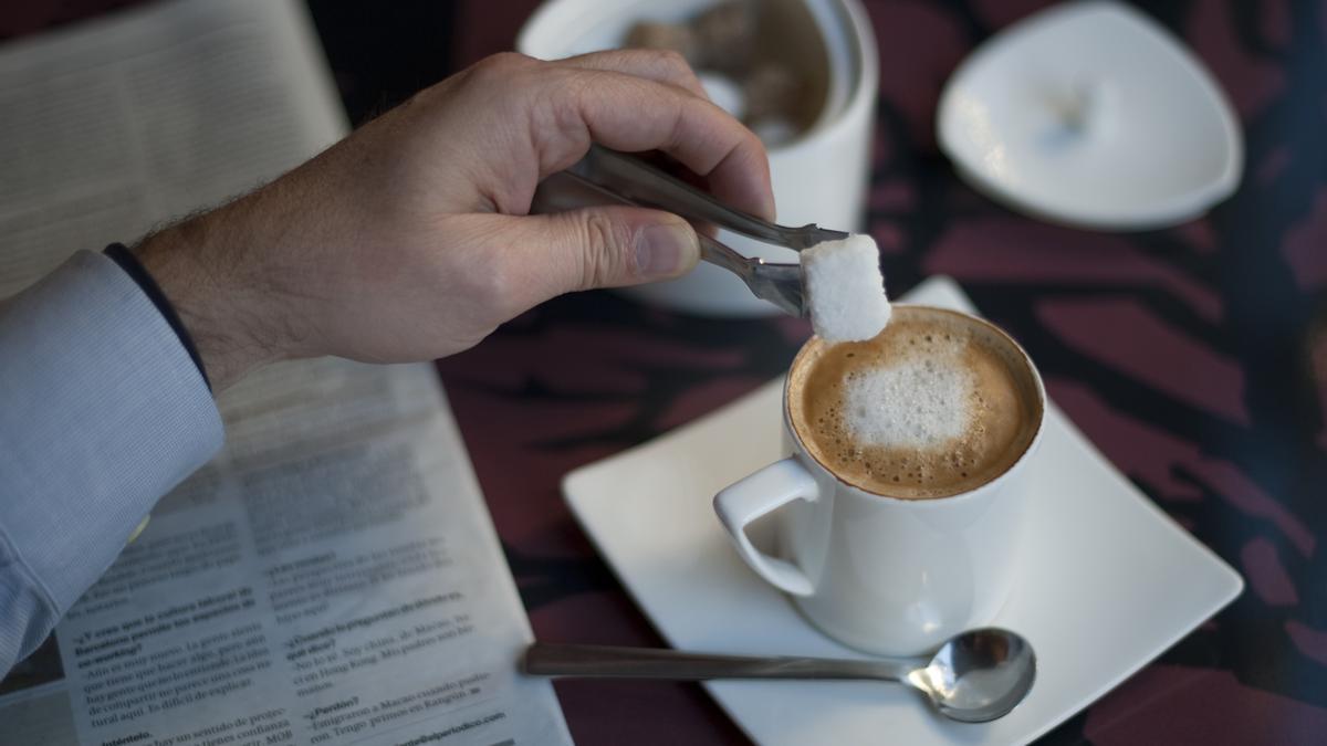 Un hombre se echa un terrón de azúcar en un café con leche en una cafetería de Barcelona.