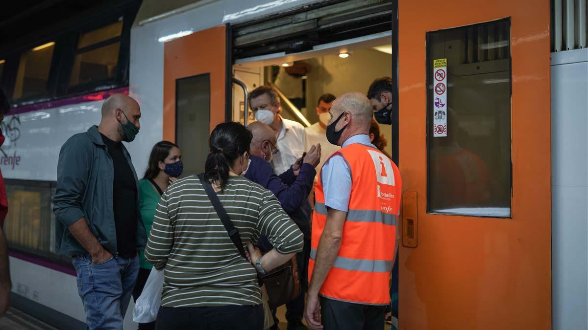 Pasajeros y un informador de Rodalies junto a un tren, en la estación de Sants