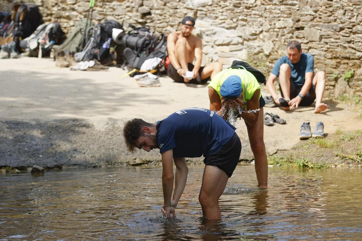 GRAF9172. ARZÚA (LA CORUÑA), 14/07/2022.- Los peregrinos descansan en un río en Ribadiso, Arzúa, para escapar de la ola de calor, este jueves en la localidad coruñesa. EFE/ Lavandeira Jr