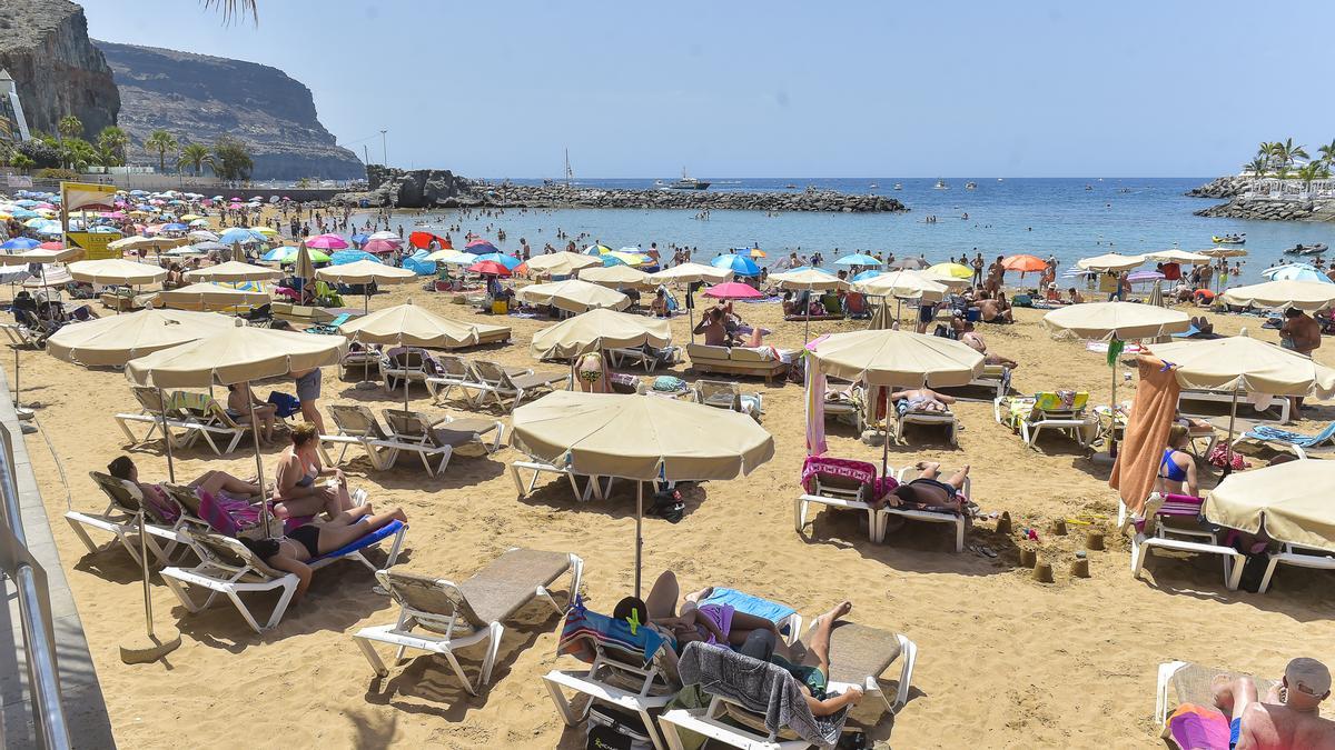 Grupos de personas toman el sol en la playa de Mogán.