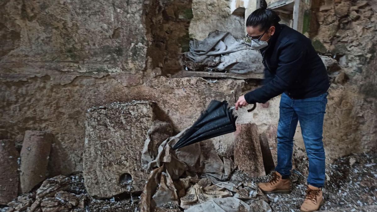 David Valiela desatapa col paragües una pieza de cantería del monasteriu de Corniana que protexó con una lona. | S. Arias