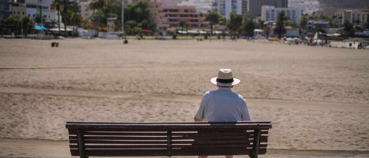 Un hombre mira desde un banco una playa desierta en Los Cristianos, al sur de Tenerife, en lo peor de la pandemia.