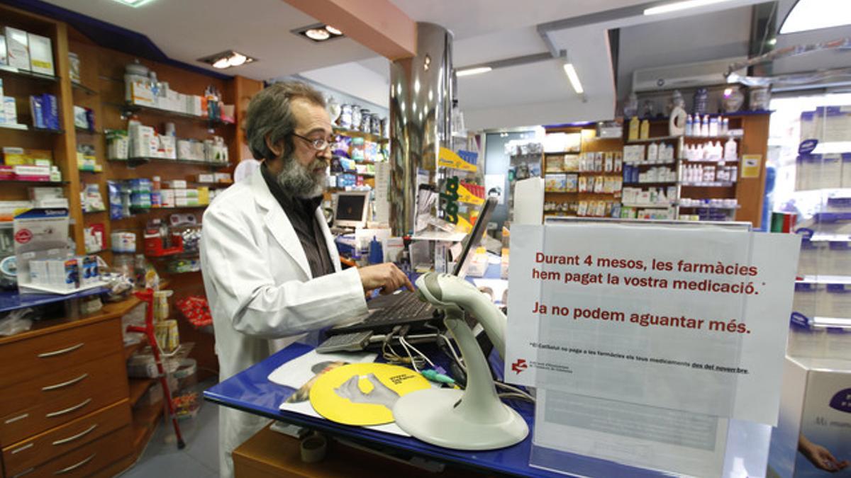 Tomás Berasategui, en su farmacia en Barcelona el pasado abril, junto a un cartel que denuncia la situación que vive el sector.