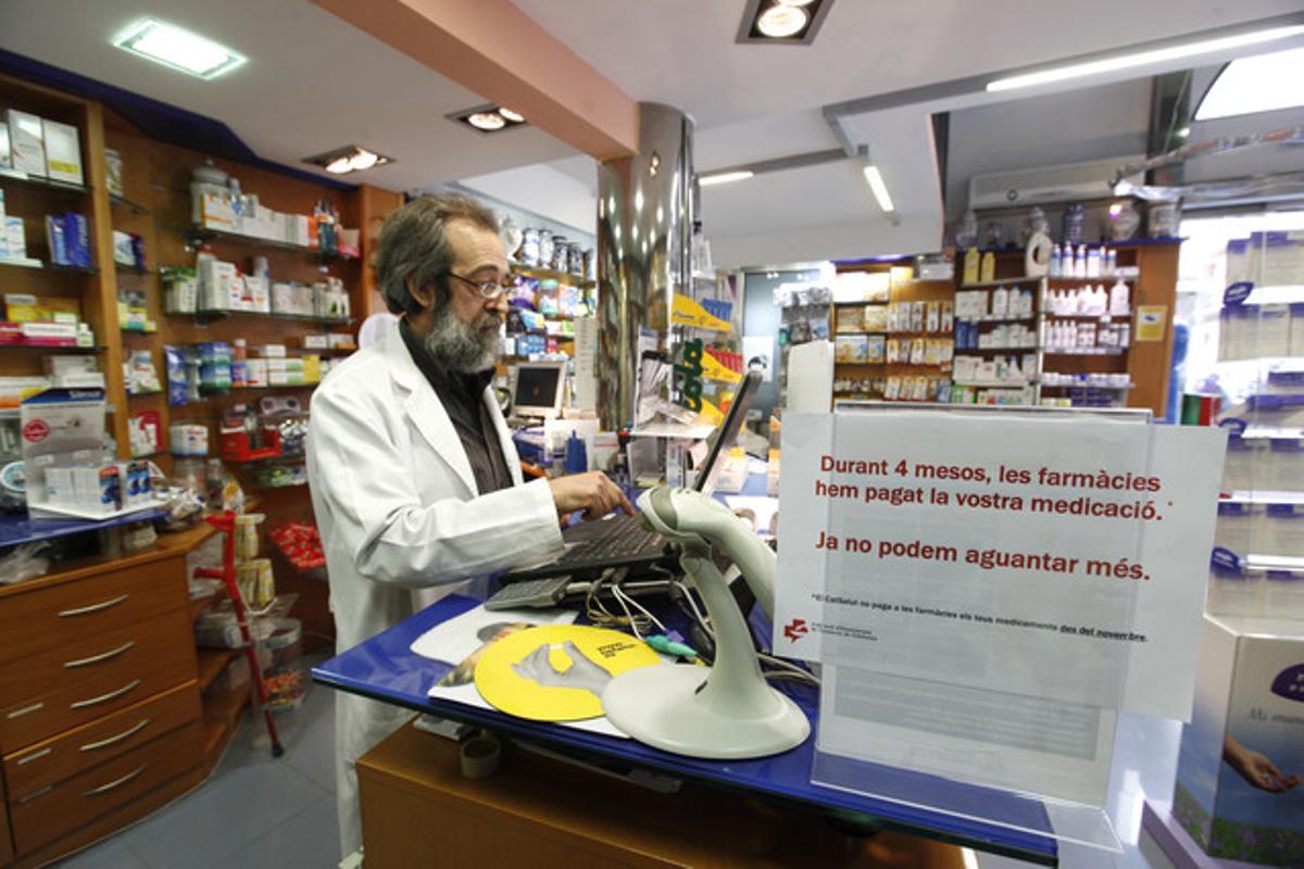 Tomás Berasategui, en su farmacia en Barcelona el pasado abril, junto a un cartel que denuncia la situación que vive el sector.