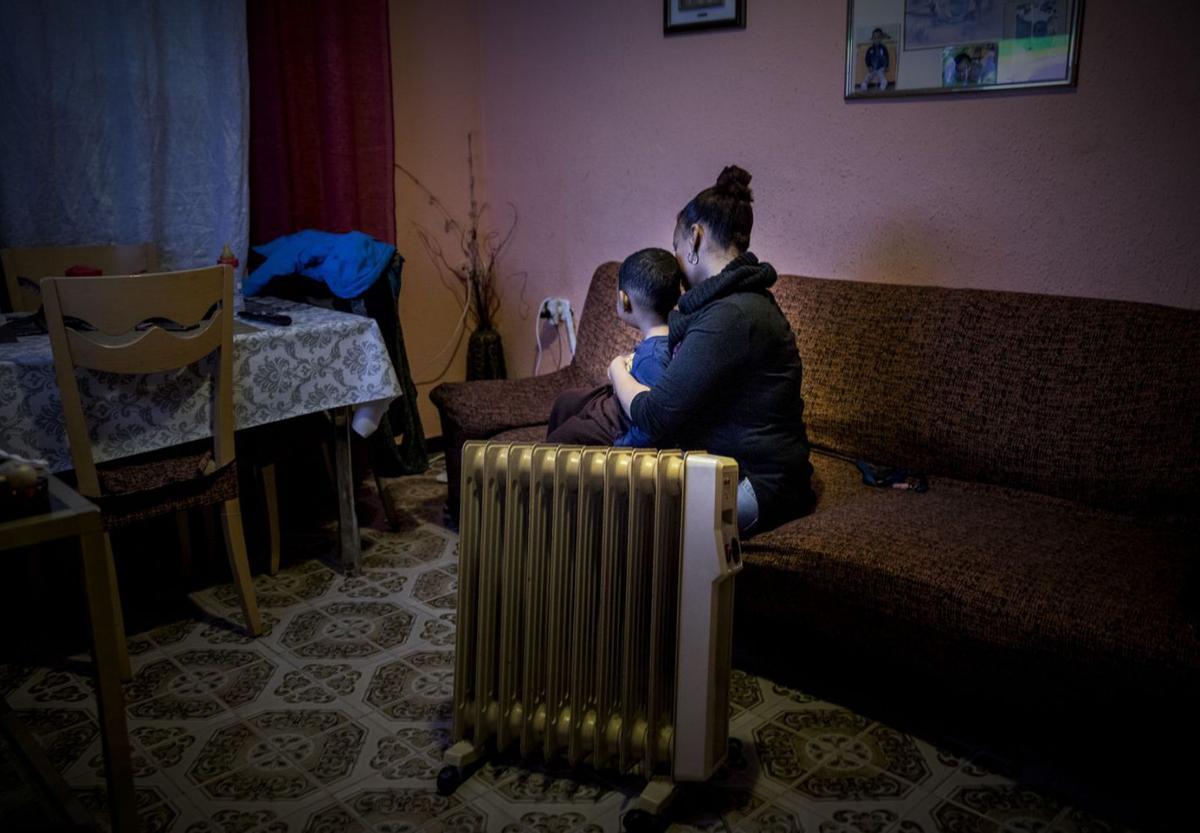 Una madre con su hijo calentándose con un radiador eléctrico.