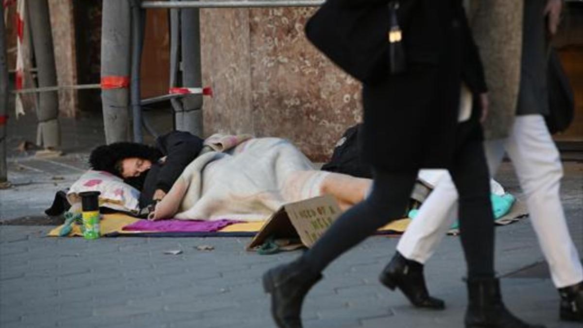 Un hombre sin hogar duerme y pide ayuda a la vez en una acera del paseo de Gràcia, el pasado noviembre.