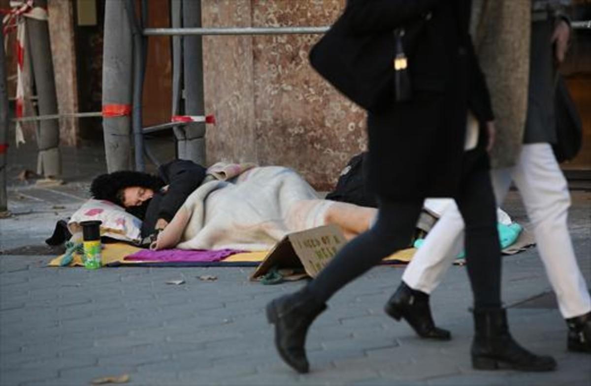 Un hombre sin hogar duerme y pide ayuda a la vez en una acera del paseo de Gràcia, el pasado noviembre.