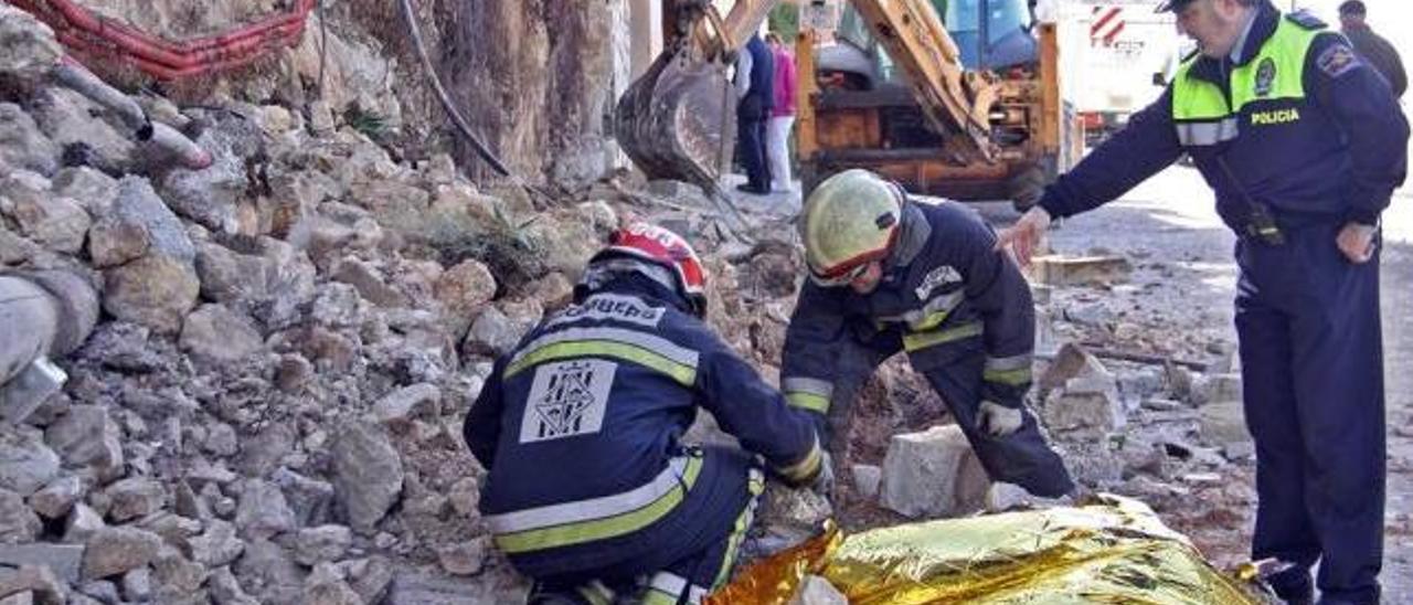 Dos bomberos y un policía, junto al cadáver de la víctima, que falleció aplastada al derrumbarse un muro en Cala Llamp (Andratx).