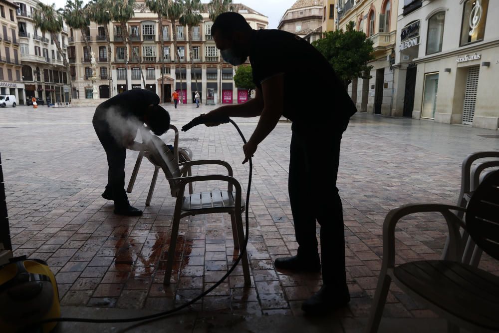 Imágenes de una lluviosa mañana de jueves en el centro de Málaga, donde al paisaje ya habitual de pocas personas y la mayoría de ellas con guantes y mascarillas se le han añadido los preparativos de bares, cafeterías y terrazas que se preparan para el inminente cambio de fase de la desescalada de la ciudad.