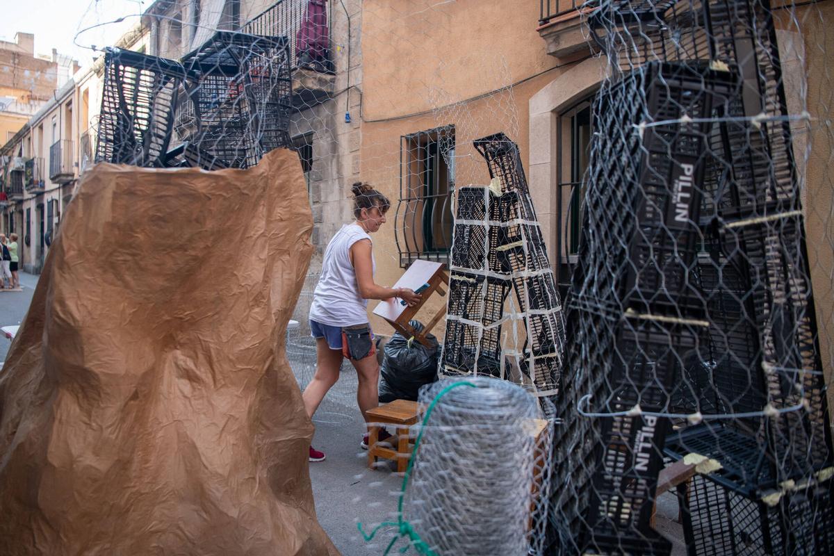 Una vecina de la calle Fraternitat D’Abaix moviendo una mesa entre las estructuras que están construyendo para decorar su calle durante las fiestas mayores de Gràcia. Este año, 5 calles del barrio se han unido bajo la temática de ‘El Señor de los Anillos’. Barcelona, 4 de agosto de 2026. Foto: Belén González / EP