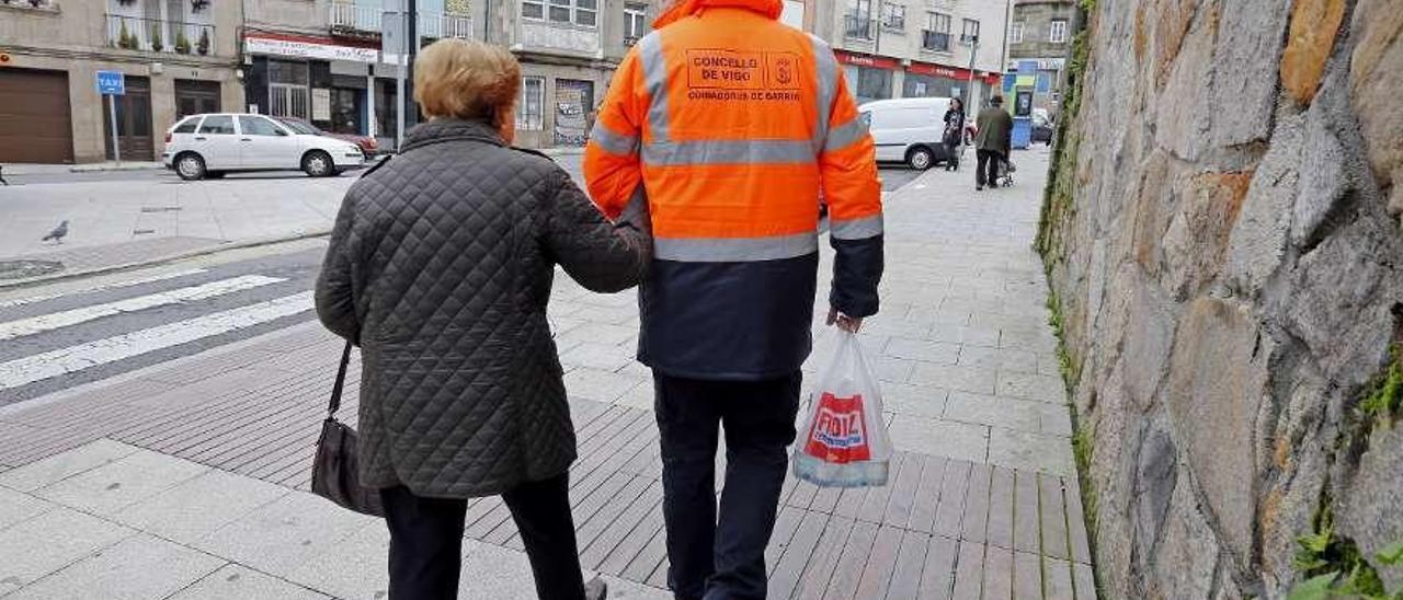 Un &quot;coidador&quot; de barrio ayuda a una anciana viguesa con la bolsa de la compra. // Marta G. Brea