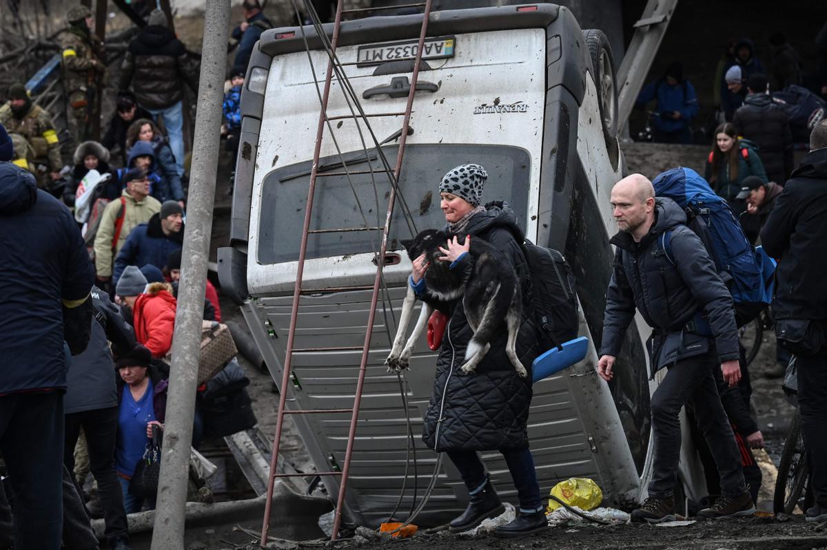 Una mujer y su perro se disponen a cruzar un puente destruido en la ciudad de Irpin, al noroeste de Kiev, durante su huida de los bombardeos en Ucrania.