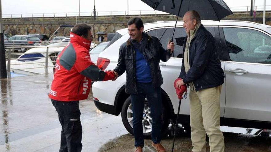 Pedro Campos saluda a Gonzalo Pita, que resguarda con un paraguas a Don Juan Carlos. // G. Santos