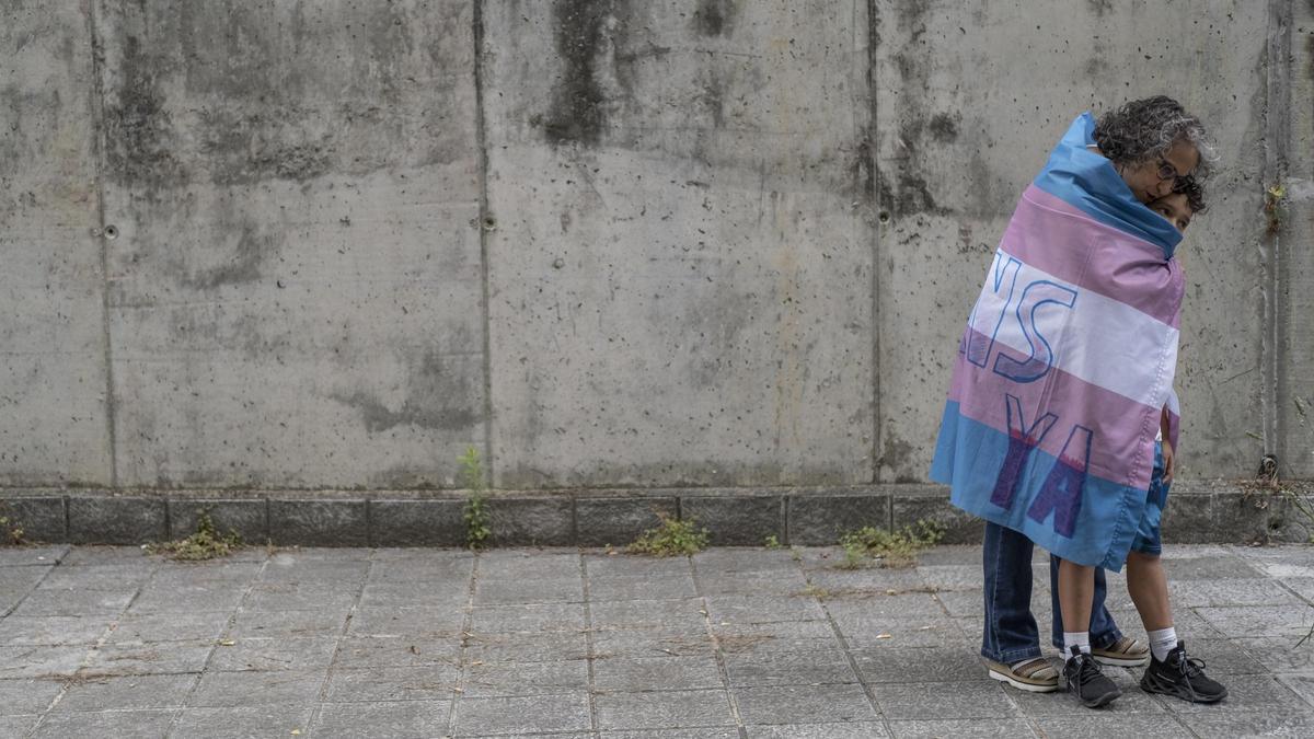 Una madre abraza a su hijo, envuelto en la bandera trans.