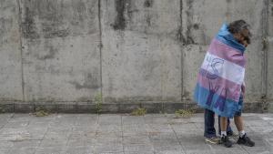 Una madre abraza a su hijo, envuelto en la bandera trans.