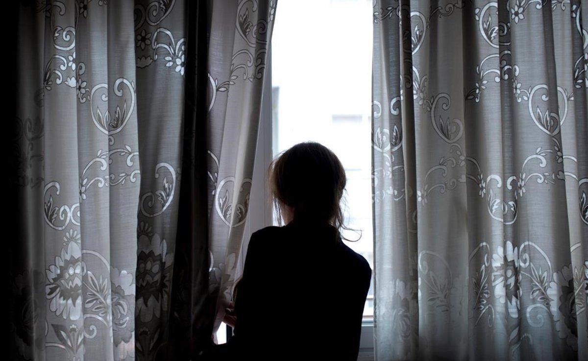 Una mujer mira por la ventana de su casa, en la que permanece confinada.